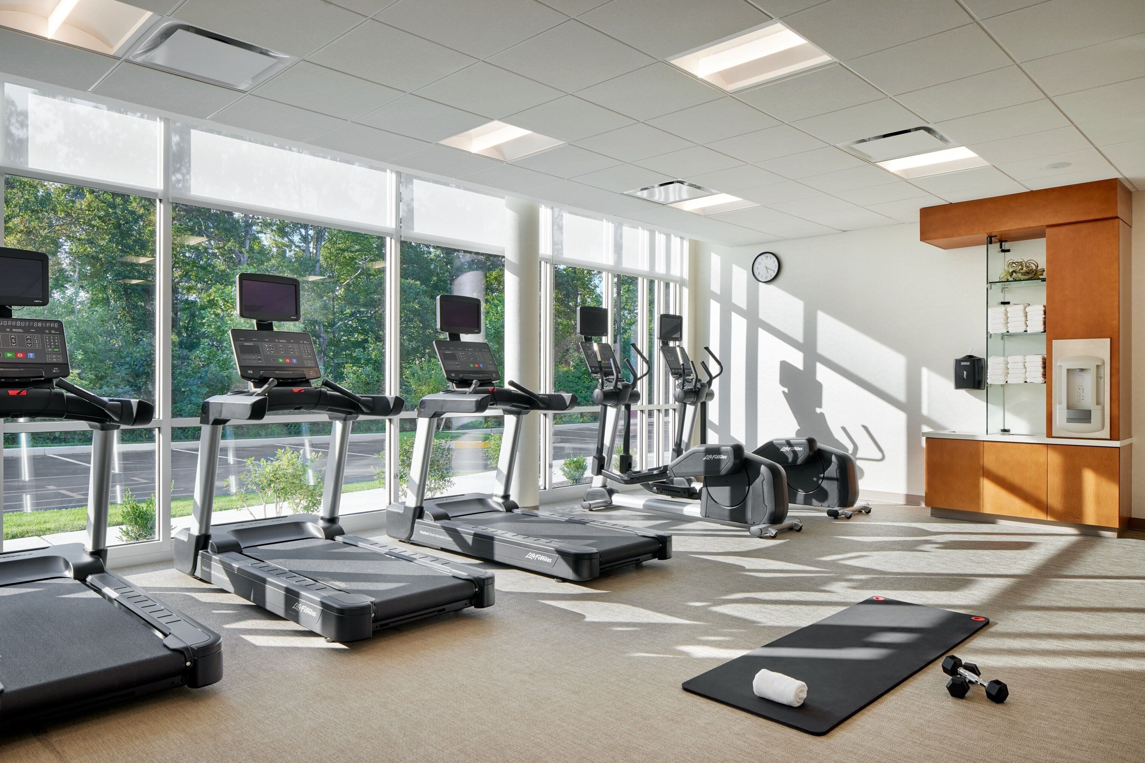 A gym with treadmills, elliptical machines, and a yoga mat.