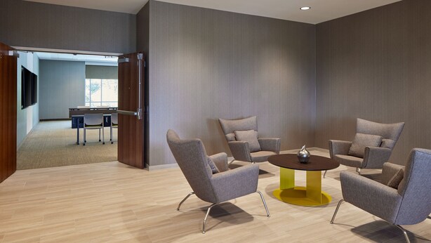 A modern conference room with four grey upholstered chairs around a yellow and brown table, wooden flooring, and a large window in the background. - Springhill Suites By Marriott Frederica (Frederica)