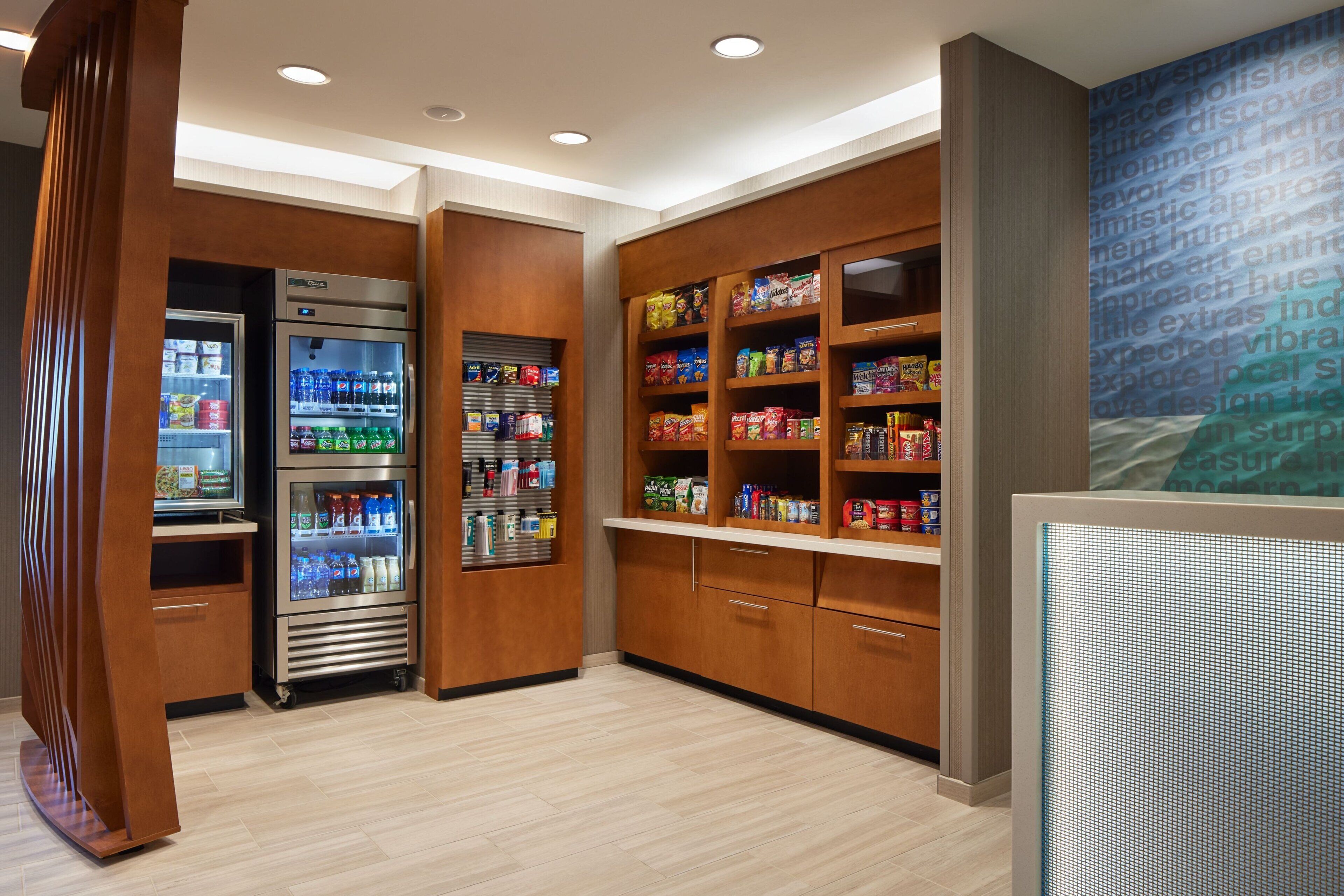 A modern kitchenette with built-in appliances, wooden cabinets, and a variety of snacks and beverages.