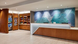 A modern reception area with a wooden reception desk, a large wall mural, and a refrigerated display case. - Springhill Suites By Marriott Frederica (Frederica)