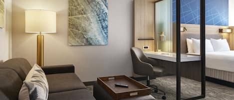 A hotel room with a sofa, a desk, a bed, a lamp, and a painting on the wall.