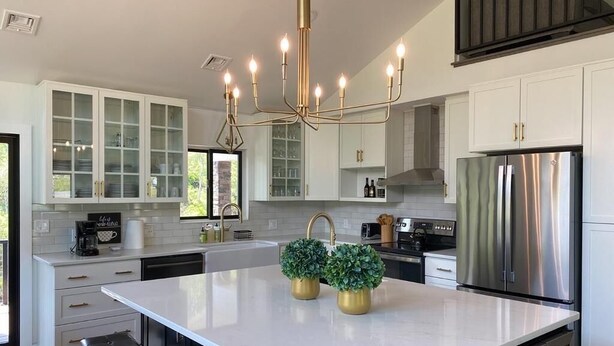 A modern kitchen with white cabinetry, a central island, stainless steel appliances, and a chandelier.
