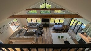 A spacious living area with a high ceiling, wooden beams, a large sofa, a dining table, and a kitchen area.