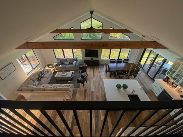 A spacious living area with a high ceiling, wooden beams, a large sofa, a dining table, and a kitchen area. - Brand New Waterfront Luxury Home, convenient to Cooperstown
All Star Village (Franklin)