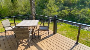 A wooden deck with wicker furniture and a table, overlooking a forested area.