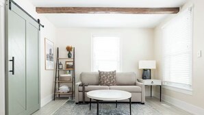 Uma sala de estar moderna com sofá, mesa de centro, mesa lateral, luminária, estante de livros e uma porta de correr.