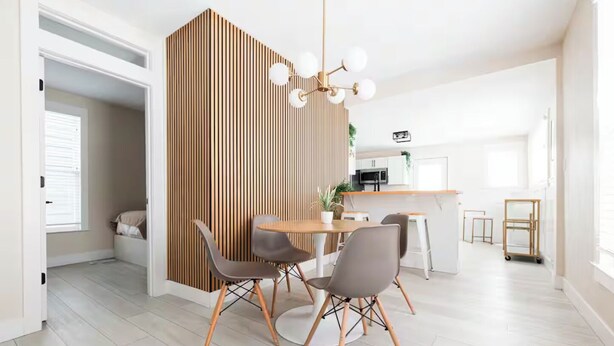 Uma área de refeições moderna com um painel de madeira, uma mesa redonda e quatro cadeiras.