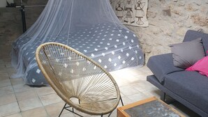 A cozy room with a bed covered in a sheer canopy, a wicker chair, a sofa, and a patterned rug. - Joli Mazet Indépendant à Louer (robiac-rochessadoule)
