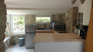 A compact kitchen with a refrigerator, microwave, and toaster. There is a window providing natural light and a view of greenery outside. - Joli Mazet Indépendant à Louer (robiac-rochessadoule)