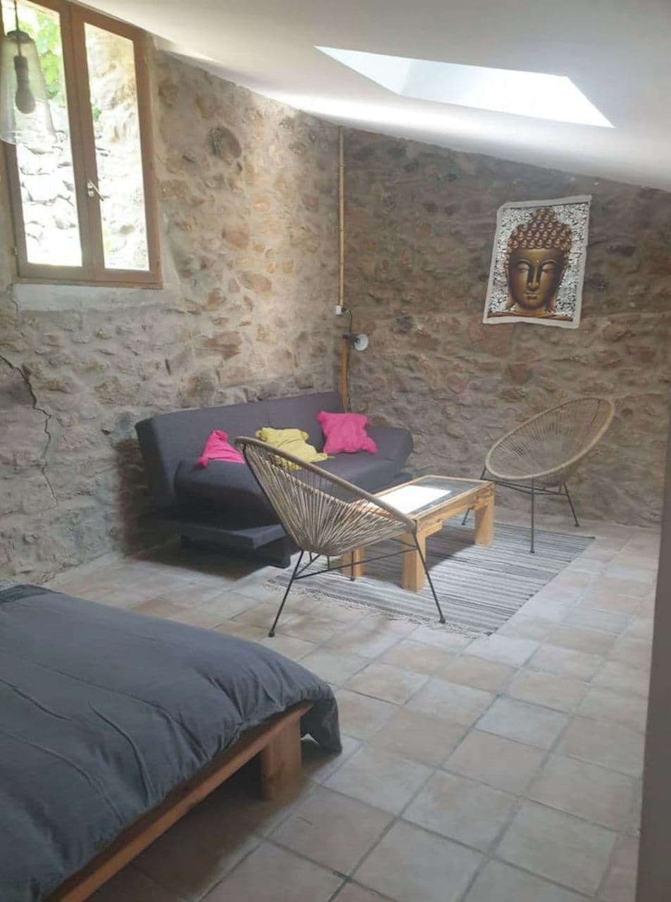 Um quarto com parede de pedra, um sofá, uma cadeira, uma cama e uma mesinha.