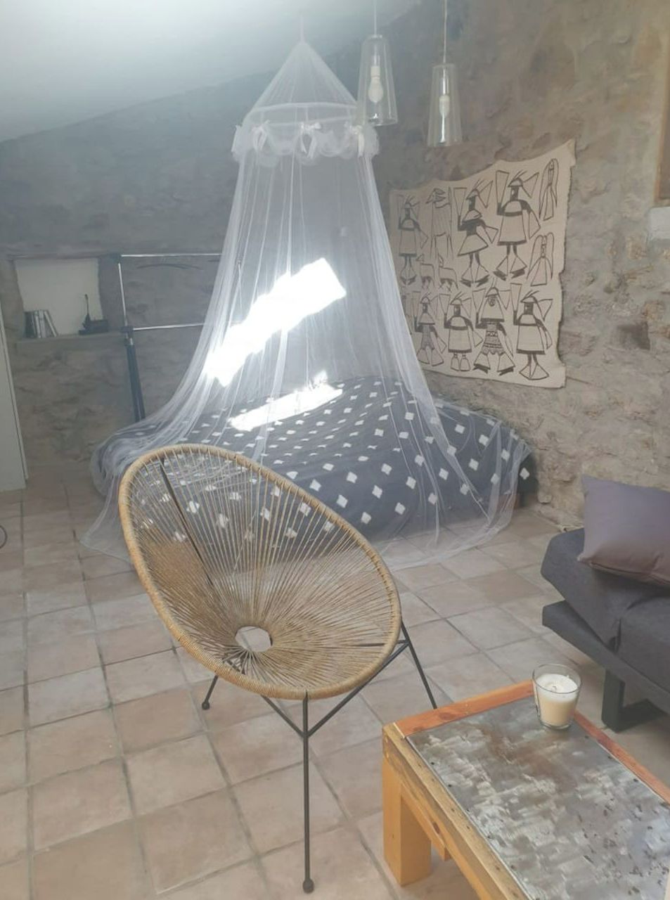 Ein gemütliches Zimmer mit einem Moskitonetz über dem Bett, einem Korbstuhl, einem Sofa und einem Tisch mit einem Glas.