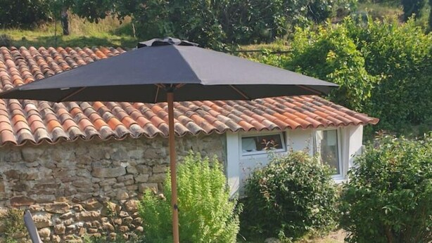 A patio with a table and chairs, a stone wall, and a tiled roof structure. - Joli Mazet Indépendant à Louer (robiac-rochessadoule)