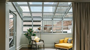 Une pièce dotée d’une grande verrière, d’un canapé jaune, d’un fauteuil, d’un lampadaire et d’une plante en pot.
