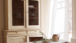 A dining area with a wooden table, chairs, a cabinet with glass doors, and a hanging light fixture.