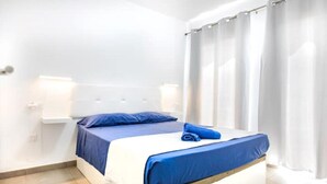 A neatly made bed with blue bedding, a white headboard, and a bedside table with a lamp.