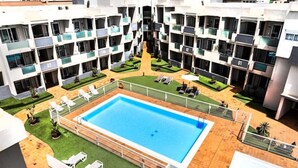 A multi-story hotel with a central swimming pool surrounded by sun loungers and a small garden area.