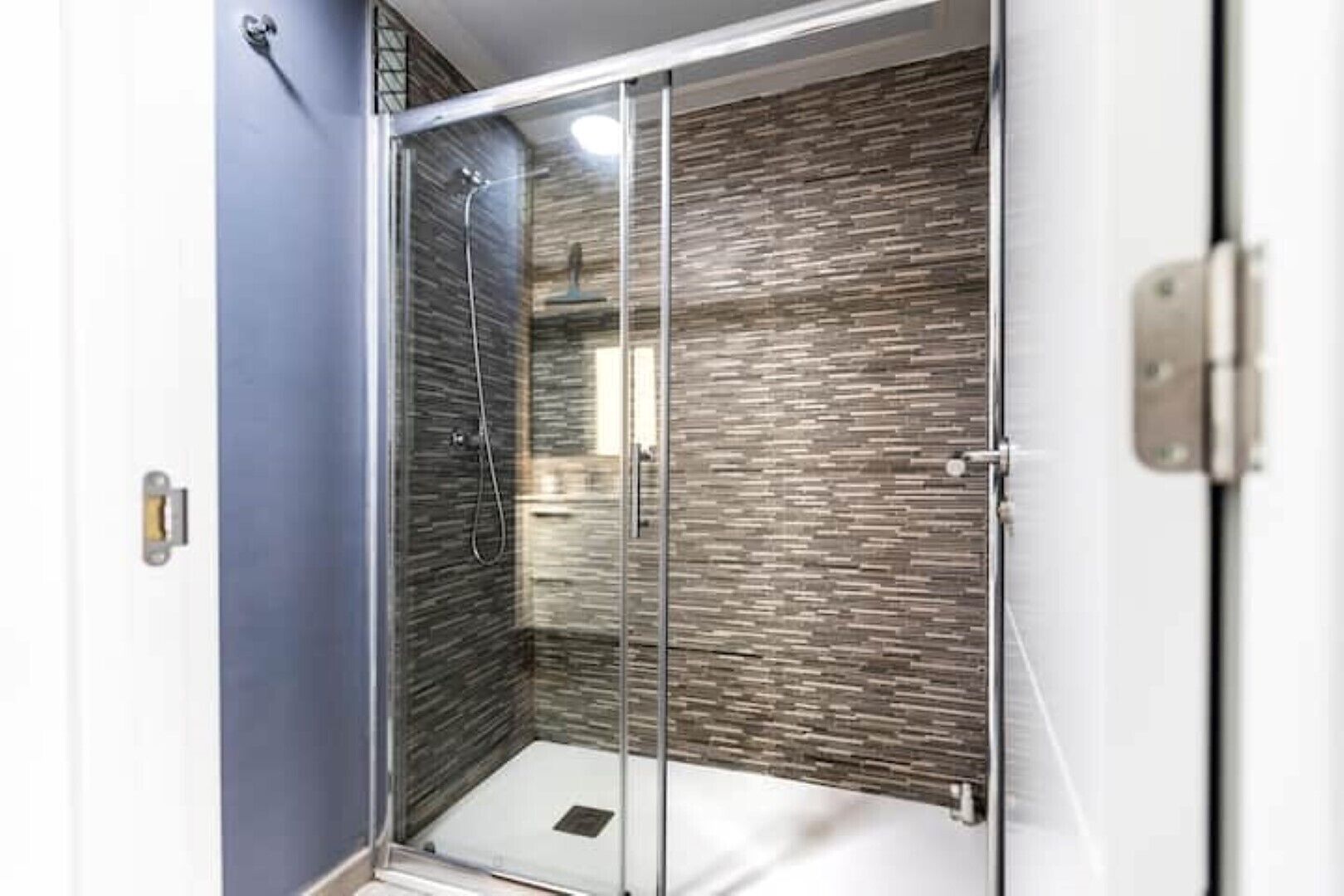 Eine Duschkabine mit Glas, einer strukturierten Wand, einem sichtbaren Abfluss und einem Türgriff.