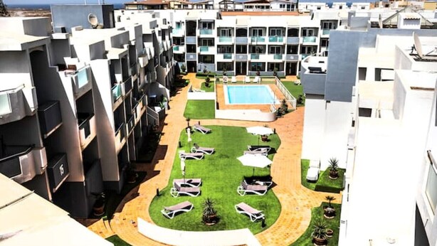 A hotel courtyard with a swimming pool, lounge chairs, and a central lawn area.