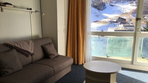Ein modernes Wohnzimmer mit einer Couch, einem runden Tisch und einem großen Fenster mit Blick auf eine verschneite Landschaft.