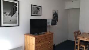 Ein kleines Zimmer mit einem Holzkleiderschrank, einem Flachbildfernseher, einer Mikrowelle und einem Esstisch mit Stühlen.