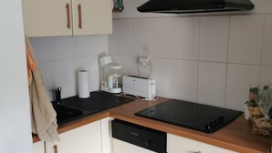 Eine kleine Küche mit weißen Schränken, einer schwarzen Dunstabzugshaube, einem integrierten Geschirrspüler und einer Holz Arbeitsplatte.