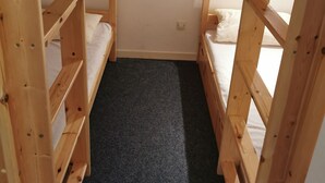 Ein schmaler Raum mit hellen Holzbettkästen, einem dunkel teppichbodenbelagten Boden und einer weißen Wand.