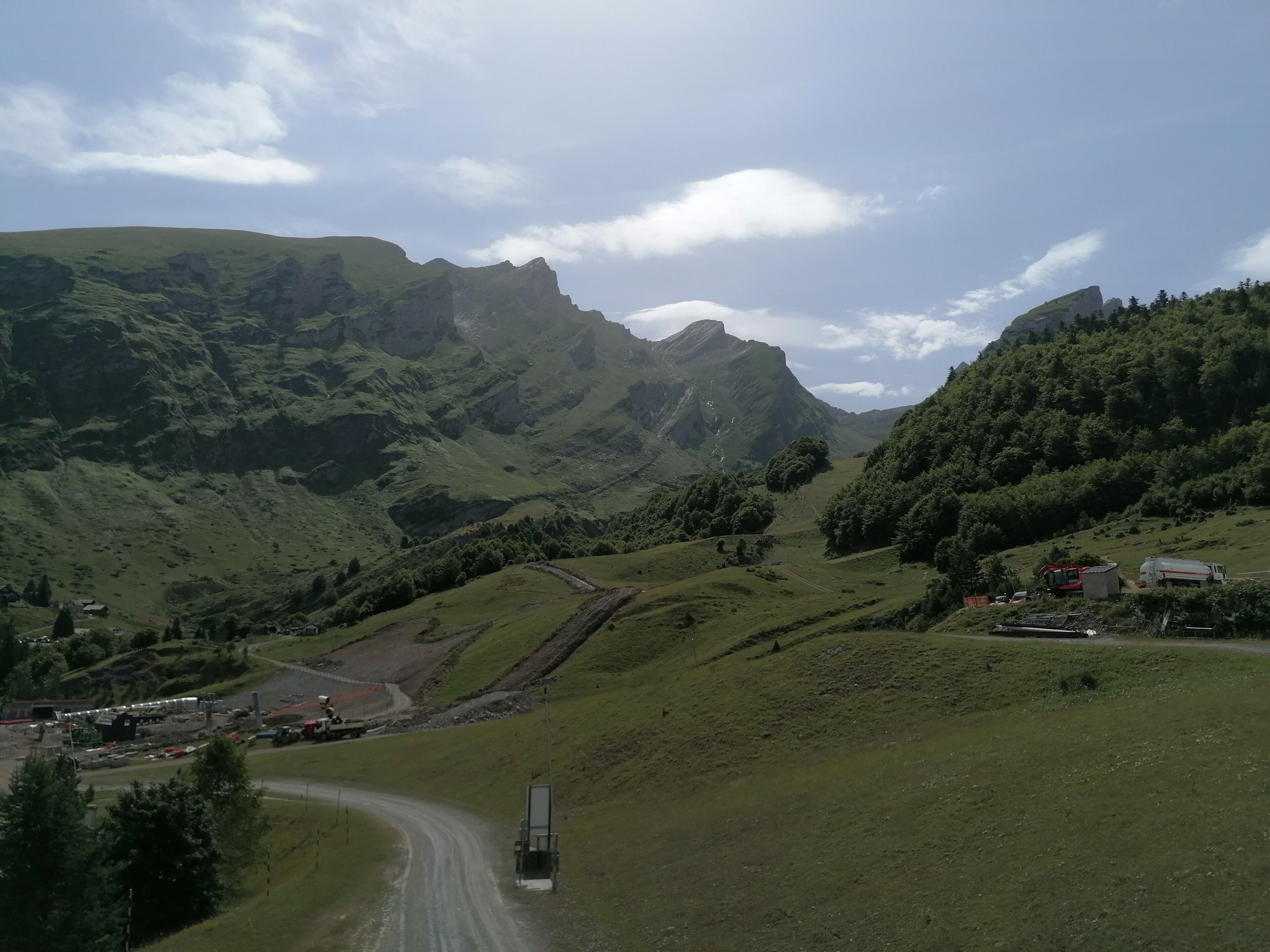 A mountainous landscape with a winding road, a truck, and a small building.