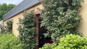Un edificio con entrada de ladrillo, rodeado de abundante vegetación y un camino de grava.