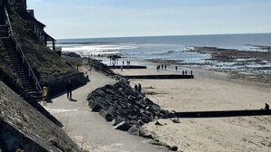 Un paseo marítimo que lleva a una playa, con un edificio histórico a la izquierda.