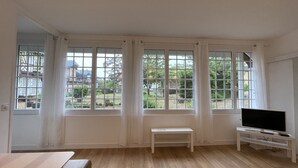 Una habitación con ventanas amplias, un televisor sobre un mueble bajo y un banco.