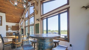 Un vaste espace dédié à la salle à manger, avec une grande table ronde entourée de tabourets en bois, un centre de table rustique en forme de tonneau et de grandes fenêtres offrant une vue sur l’extérieur.