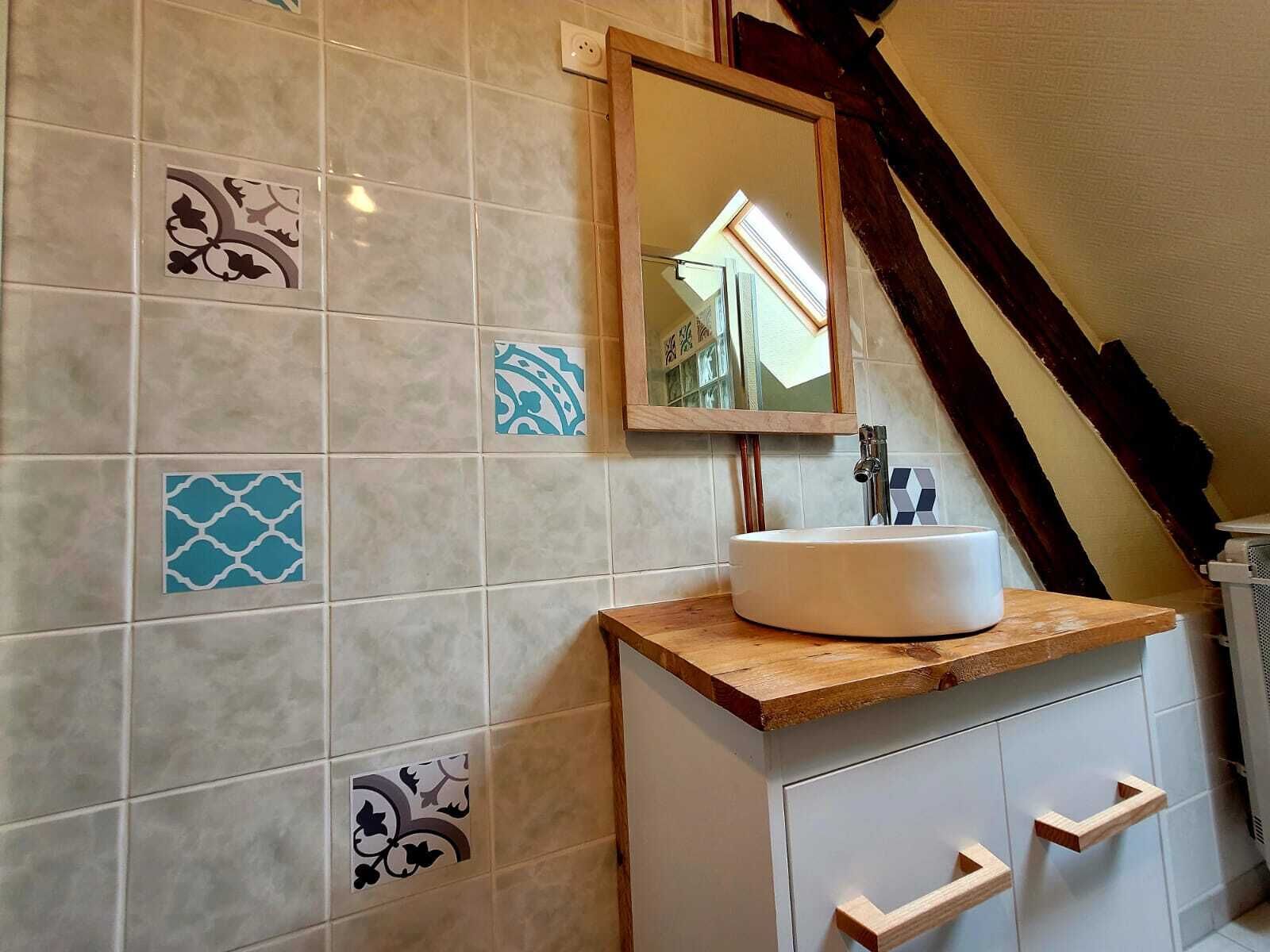 Une salle de bain avec un lavabo blanc, un plan de toilette en bois et des murs carrelés présentant différents motifs.