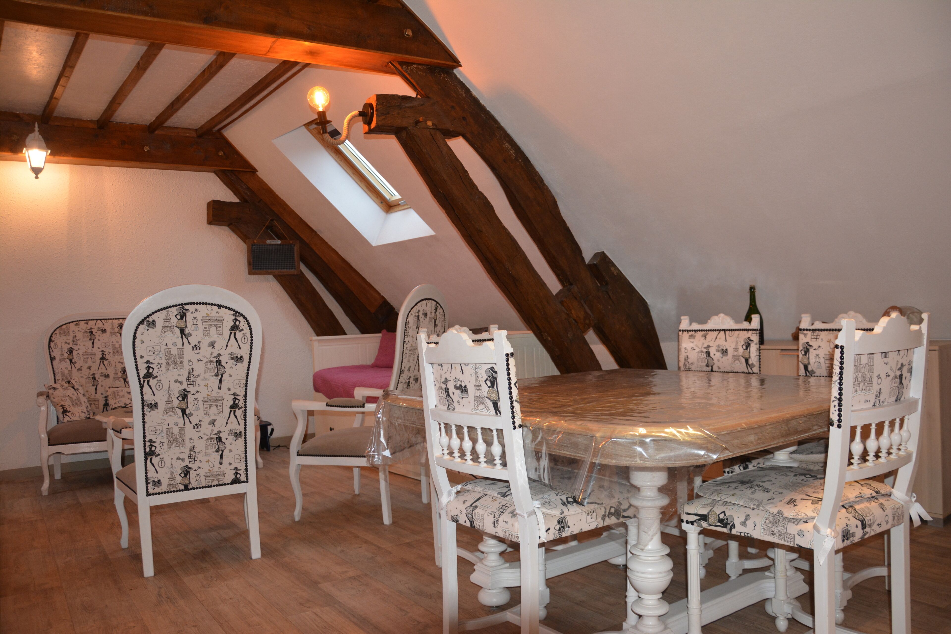 Un coin repas avec une table et des chaises en bois, un plafond en pente avec des poutres apparentes et une petite fenêtre.