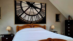 Un dormitorio con un gran reloj de pared, cama de madera, dos mesitas de noche con lámparas y un aparador oscuro.