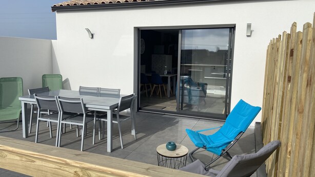 An outdoor patio with a table and chairs, a blue folding chair, and a wooden fence. - Pour 4 Pers Plein Soleil, Gd Terrasse sur Toiture (L'Aiguillon-la-Presqu'île)