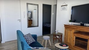 A living room with a blue sofa, a television, a wooden cabinet, and a small round table with a cup. - Pour 4 Pers Plein Soleil, Gd Terrasse sur Toiture (L'Aiguillon-la-Presqu'île)