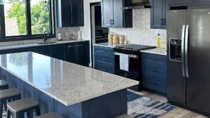 A modern kitchen with dark cabinets, a large island, and a stainless steel refrigerator. - NEW House on Pristine Shell Lake! Right off the ATV/Snowmobile trails! (Shell Lake)