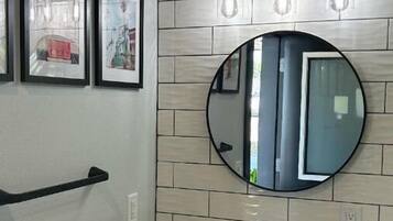 Une salle de bain avec un lavabo blanc, un miroir rond et trois luminaires placés au-dessus du miroir.