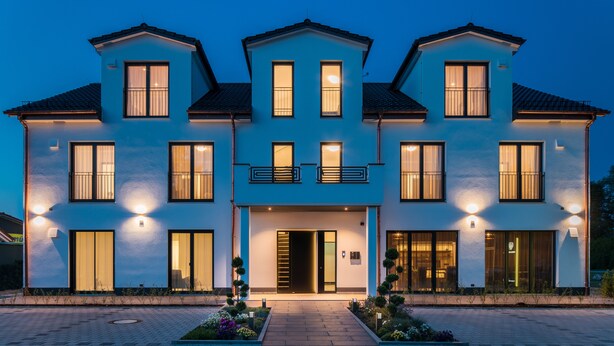 A modern two-story building with a central entrance, multiple windows, and a well-lit facade. - Herzl Hotel bei Erding (Forstern)