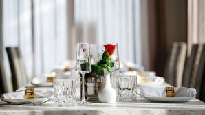 A dining table set with crystal glassware, a white vase with a red rose, and gold decorative elements. - Herzl Hotel bei Erding (Forstern)