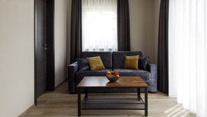 A modern living room with a dark-colored sofa, a wooden coffee table, and a bowl of fruit. - Herzl Hotel bei Erding (Forstern)