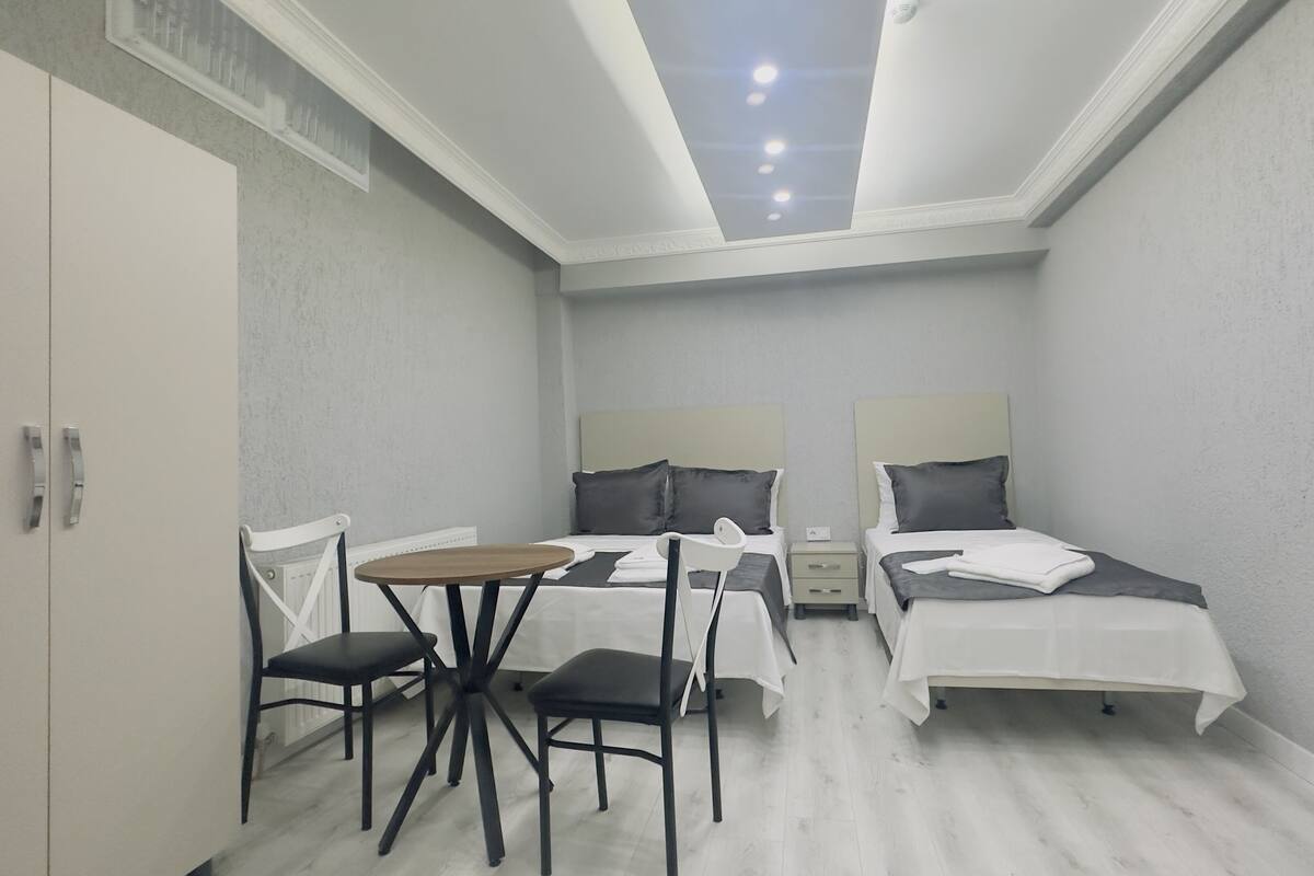 A small, modern bedroom with two single beds, a small table, and two chairs.