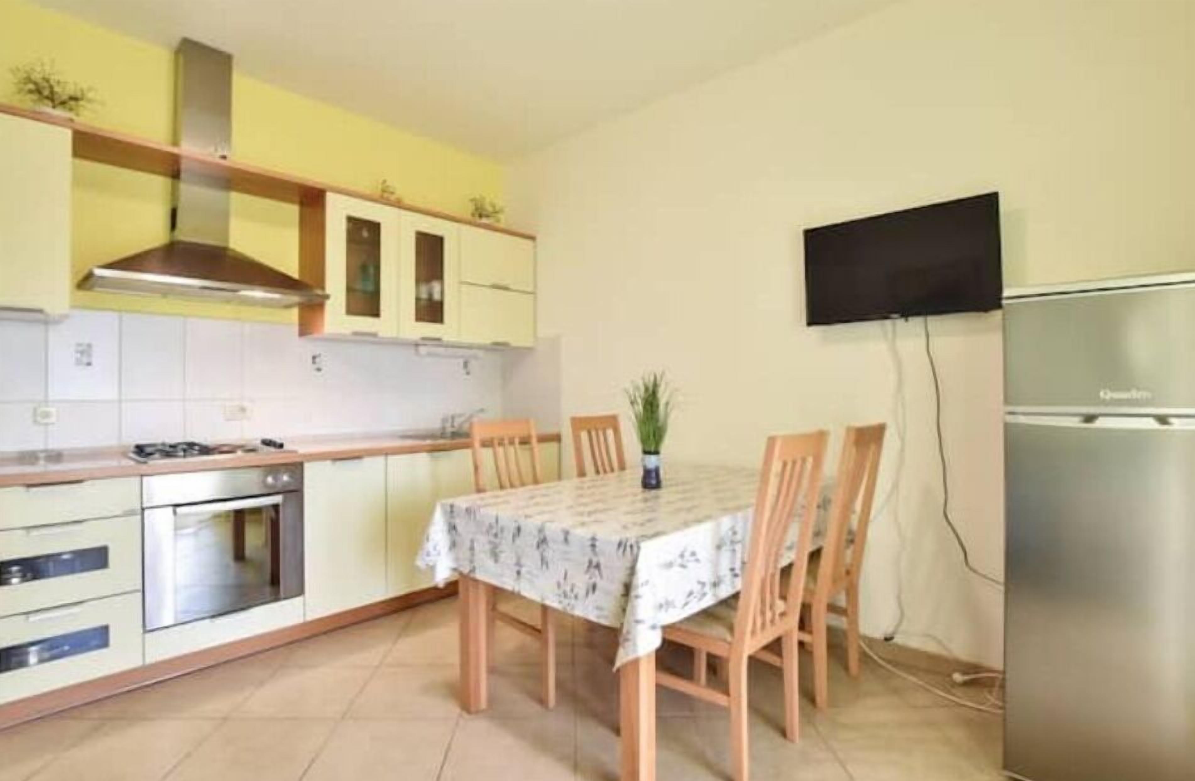 A compact kitchen with a dining table, chairs, a stove, oven, and a TV mounted on the wall.