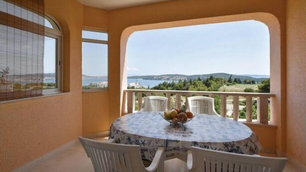 En balkon med et bord og stole, havudsigt og et vindue med gardin.