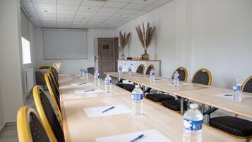 A conference room with a long table, chairs, water bottles, pens, and a projector screen.
