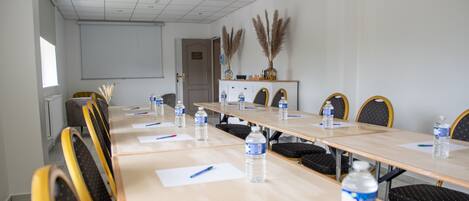 A conference room with a long table, chairs, water bottles, pens, and a projector screen.