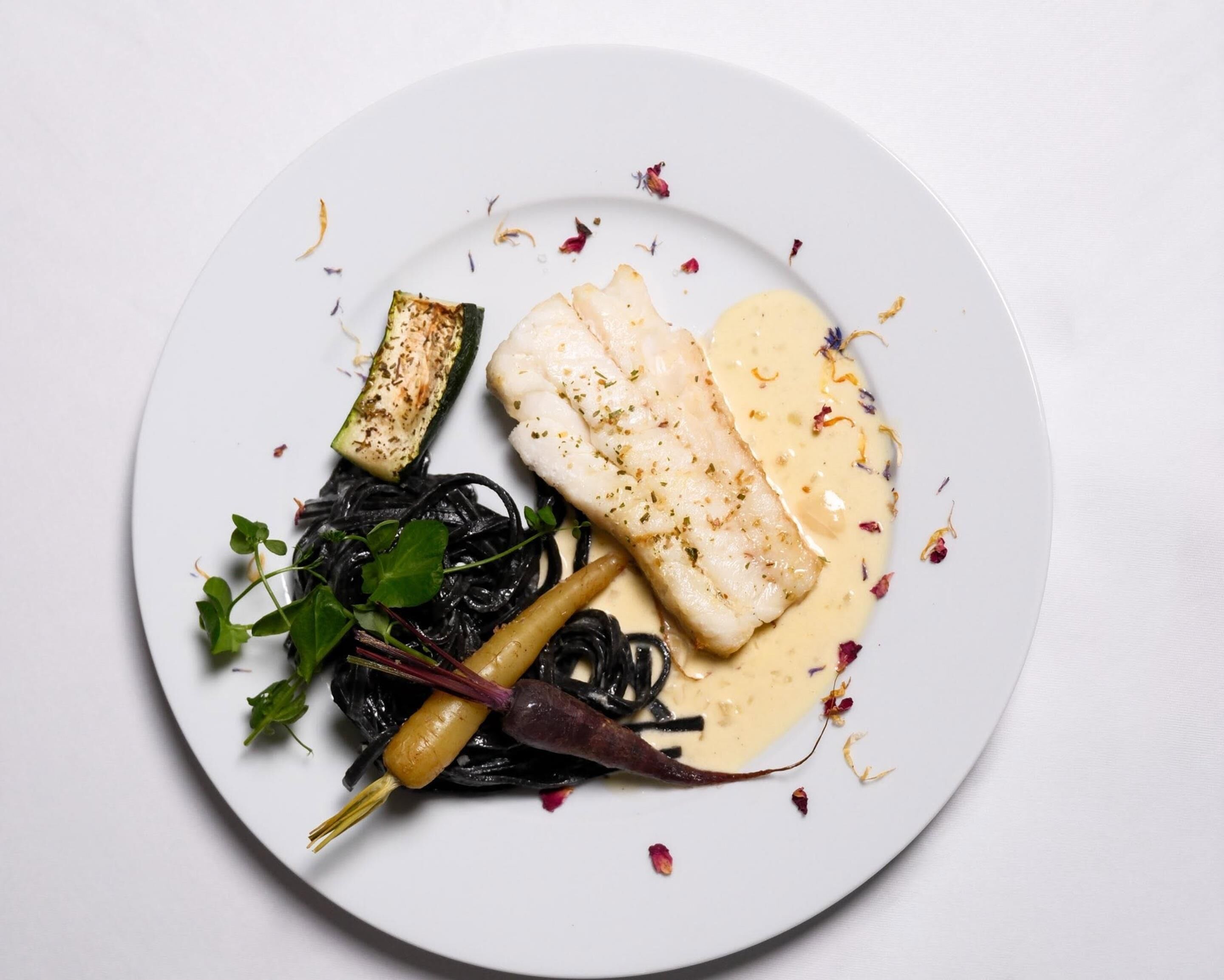 Un plato con pescado, verduras y salsa cremosa.