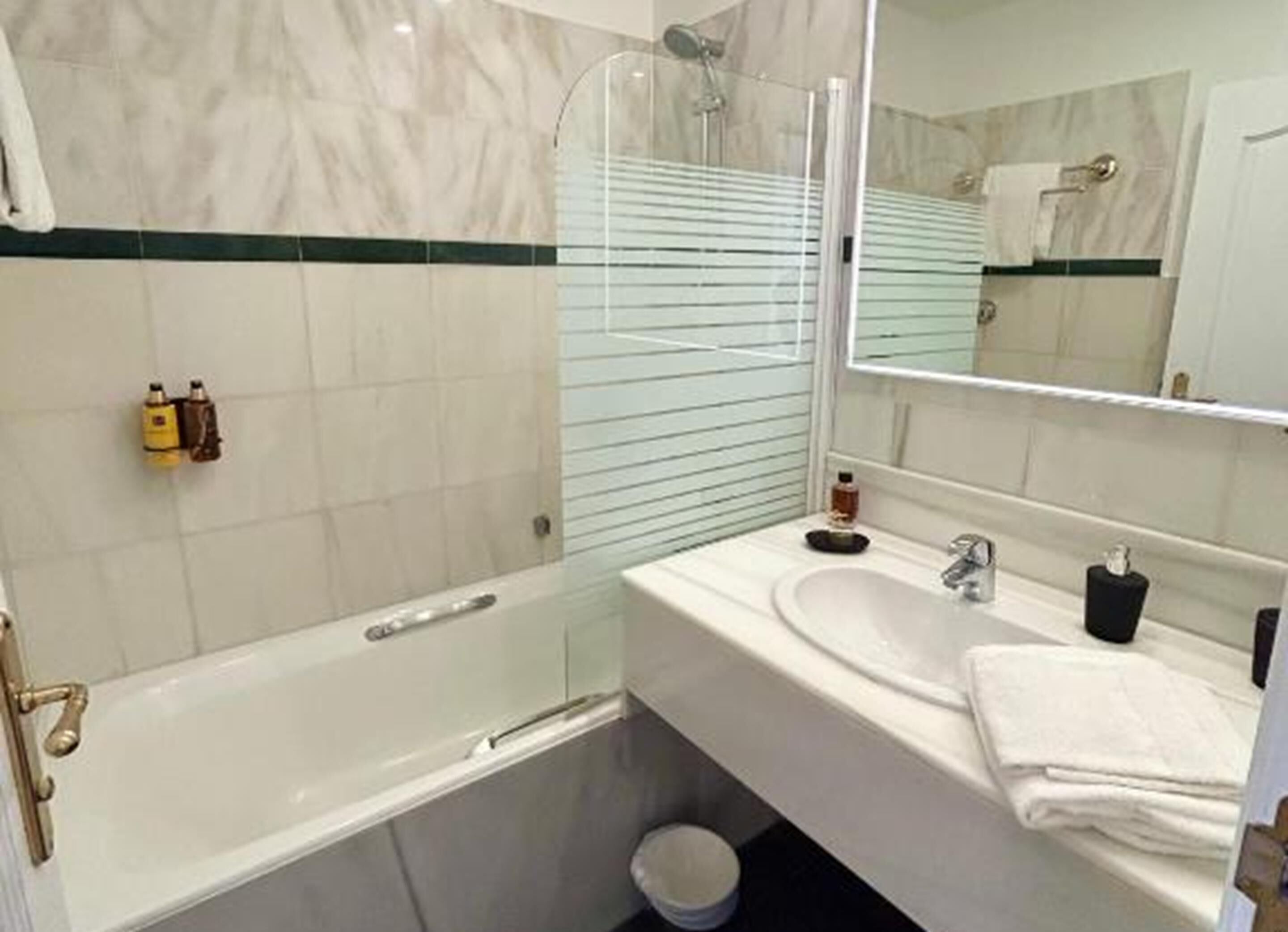 Ein Badezimmer mit Duschkabine aus Glas, einem weißen Waschbecken, einem Spiegel und einem Handtuchhalter.