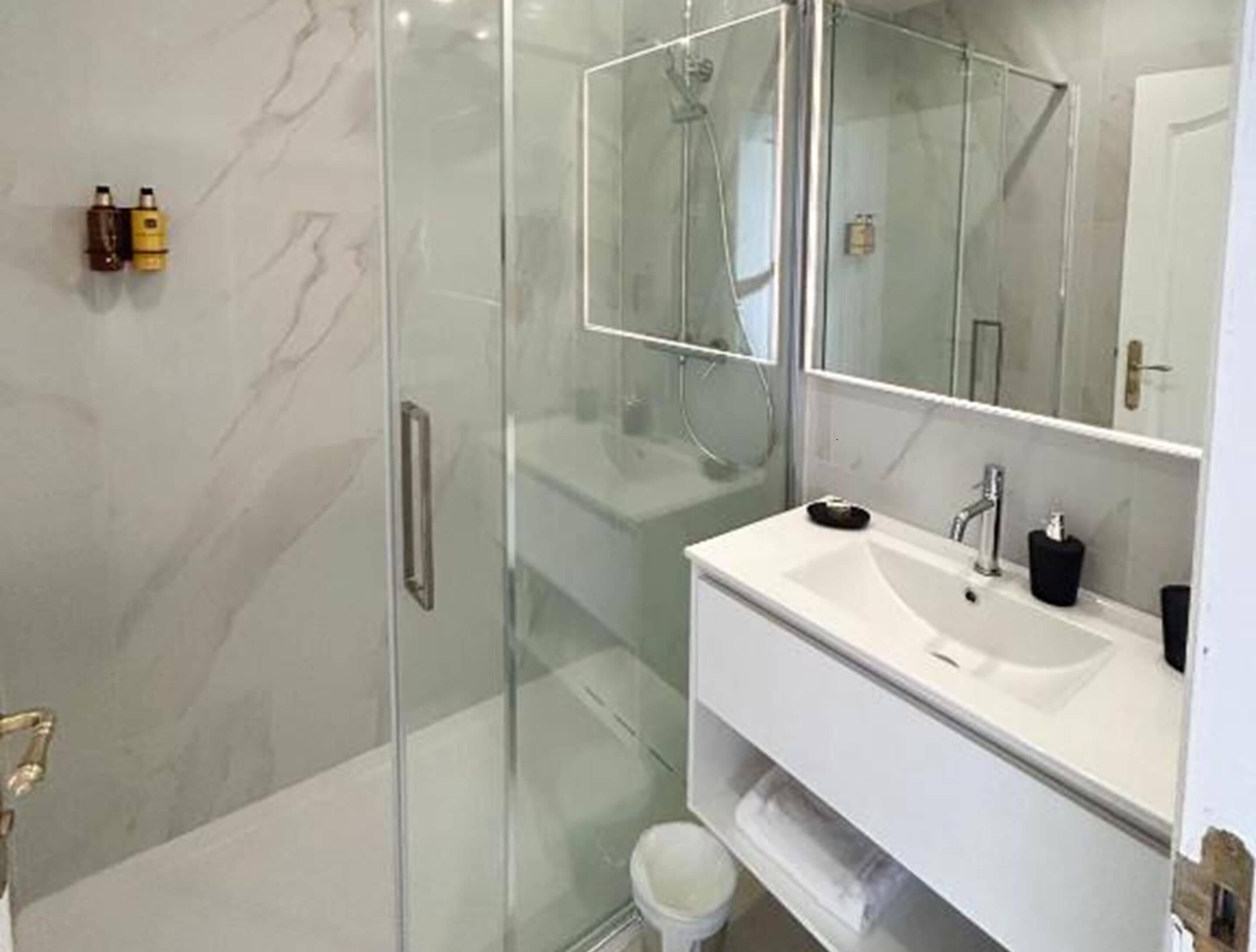 A modern bathroom with a glass shower enclosure, a white sink with a mirror, and toiletries on the wall.