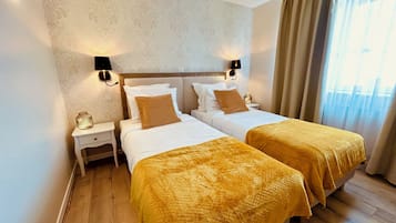 A hotel room with two beds, a nightstand, a lamp, and a window with curtains.